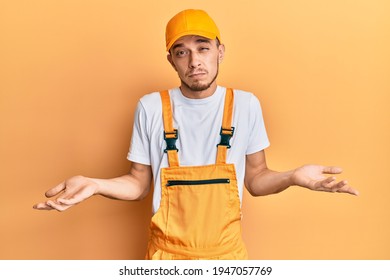 Hispanic Young Man Wearing Handyman Uniform Clueless And Confused With Open Arms, No Idea Concept. 