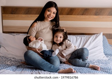 Hispanic Young Mom Hugging Her Daughters In Bed. Happy Loving Family, Small Family Home Portrait.