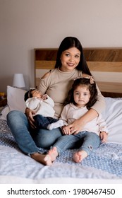 Hispanic Young Mom Hugging Her Daughters In Bed. Happy Loving Family, Small Family Home Portrait.