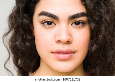 Hispanic Young Woman With Curly Hair And A Natural Beautiful Face Looking At The Camera. Close Up Of A Female Beauty And Skin Care Model 