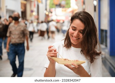 Hispanic young woman eating takoyaki at Dotonbori street in Osaka, Japan.