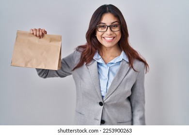 Hispanic young woman holding take away bag looking positive and happy standing and smiling with a confident smile showing teeth  - Shutterstock ID 2253900263