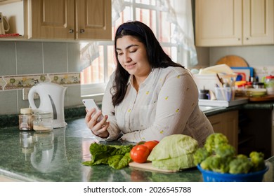 Hispanic young woman looking for recipes on the phone- young man preparing fresh salad - healthy life
