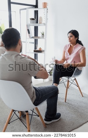 Hispanic young woman psychologist with male patient telling about mental problems while doctor is listening and making notes. Psychotherapy concept in Mexico Latin America