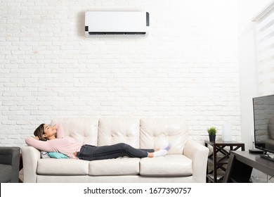 Hispanic Young Woman Sleeping Below Mini Split On Sofa In Living Room At Home