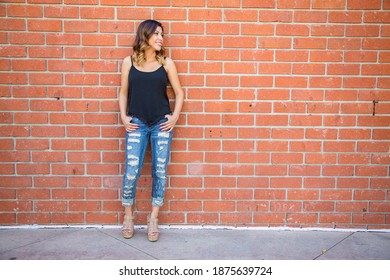Joven hispana frente a una pared de ladrillo rojo con jeans rasgados 