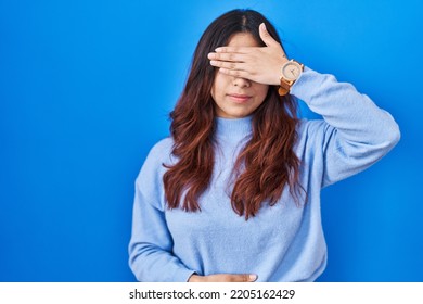 Hispanic Young Woman Standing Over Blue Background Covering Eyes With Hand, Looking Serious And Sad. Sightless, Hiding And Rejection Concept 