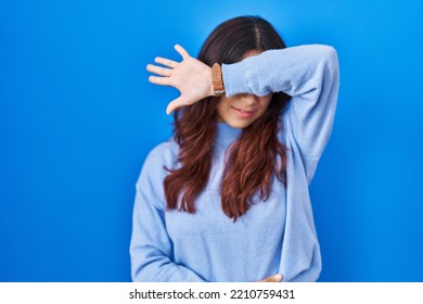 Hispanic Young Woman Standing Over Blue Background Covering Eyes With Arm, Looking Serious And Sad. Sightless, Hiding And Rejection Concept 