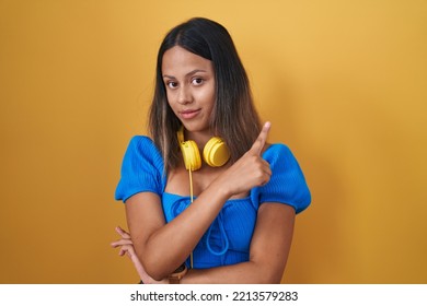 Hispanic Young Woman Standing Over Yellow Background Pointing With Hand Finger To The Side Showing Advertisement, Serious And Calm Face 