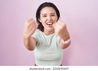 Hispanic young woman standing over pink background angry and mad raising fists frustrated and furious while shouting with anger. rage and aggressive concept.  - Shutterstock ID 2310295497
