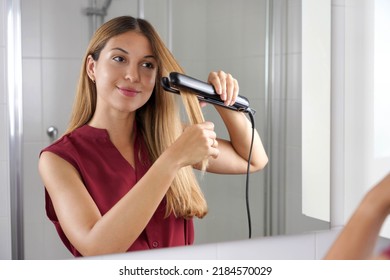 Hispanic Young Woman Using Steam Straightener To Style Hair In The Mirror On Bathroom