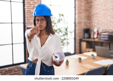 Hispanic Young Woman Wearing Architect Hardhat At Office Pointing With Finger To The Camera And To You, Confident Gesture Looking Serious 