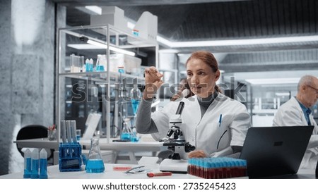 Histology technician using compound microscope for detailed cellular analysis research. Female materials scientist doing tissue sample examination inside modern laboratory facility, camera A
