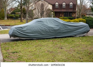 Historic Antique Muscle Car In The Driveway Of A Suburban House Completely Covered With A Gray Car Protection Cover