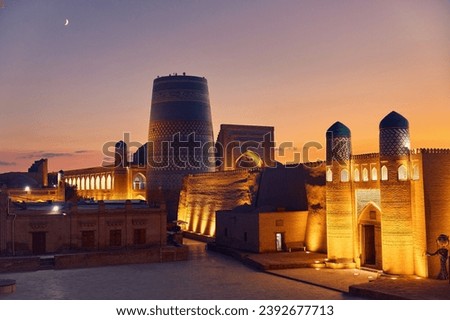Historic architecture of Kalta Minor minaret old at square and Castle gate with illumination at sunset in Itchan Kala inner town of the city of Khiva, Uzbekistan. 