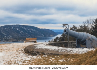 Historic artillery overlooking serene Norwegian fjord landscape in winter, featuring snow-dusted ground and distant mountains - Powered by Shutterstock