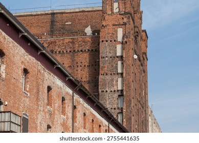 Historic brick structure features a weathered facade and large windows, set against a clear blue sky in an urban environment