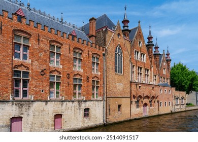 Historic buildings with step gables line a canal in Bruges, Belgium. The red brick structures feature turrets, towers, and gabled roofs, showcasing a rich architectural heritage. - Powered by Shutterstock