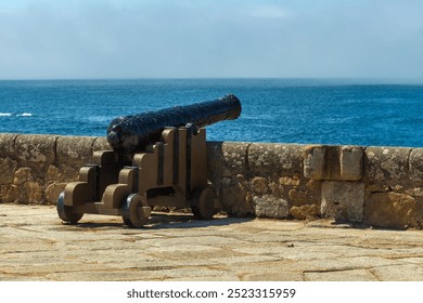 A historic cannon mounted on a stone fort wall overlooking the ocean, with clear blue skies in the background - Powered by Shutterstock