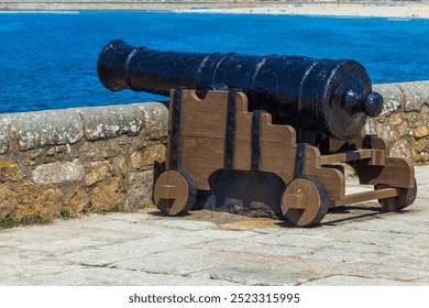 A historic cannon mounted on a stone fort wall overlooking the ocean, with clear blue skies in the background - Powered by Shutterstock