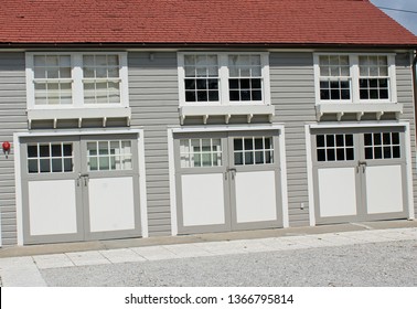 Historic Caretaker Garage With Red Shingle Roof And Three Garage Doors With Double Hung Windows Over Them. Garage Bypass Doors Have Decorative Corbels Overhead. 
