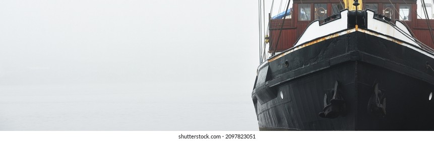 Historic Cargo Boat Moored To A Pier, In A Thick White Morning Fog, Close-up. Kiel, Germany. Transportation, Fishing, Sailing, Logistics, Industry, Traditional Craft, Past, History. Panoramic Image