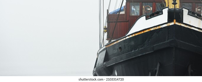 Historic Cargo Boat Moored To A Pier, In A Thick White Morning Fog, Close-up. Kiel, Germany. Transportation, Fishing, Sailing, Logistics, Industry, Traditional Craft, Past, History. Panoramic Image