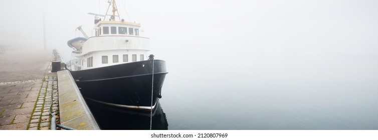 Historic Cargo Boat Moored To A Pier, In A Thick White Morning Fog, Close-up. Kiel, Germany. Transportation, Fishing, Sailing, Logistics, Industry, Traditional Craft, Past, History. Panoramic Image