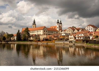 Historic center of city Telč, UNESCO, World Heritage Site, Vysočina region, Czechia. View across the pond. Sunny. Reflection of buildings on the water surface. Contrasting sky. European architecture.