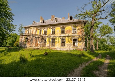 A historic, destroyed palace - the former seat of a magnate family. A dilapidated old historical building standing in a park among green plants in May development . 
