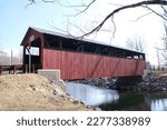 Historic Frazier red wooden covered bridge over Little Muncy Creek in Lycoming County Pennsylvania built in 1888 against blue cloud sky.  You can drive through it today.  Built in the Burr Arch style.