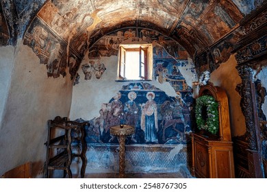 Historic frescoes and a small altar with natural light illuminating the aged walls inside Mardaki Monastery in Messinia, Greece, showcasing Byzantine art. - Powered by Shutterstock