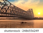 Historic Howrah bridge on the river Ganges with a view of a fishing boat at sunrise in Kolkata, India