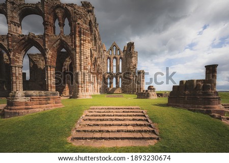 The historic landmark 7th century ruins of Whitby Abbey perched atop East Cliff north Yorkshire, England with a dark, moody sky.