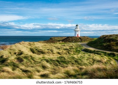 The historic landmark lighthouse at  Waipapa Point surrounded by grassy sand dunes on a sunny and cloudy day on the Dunedin coast - Powered by Shutterstock