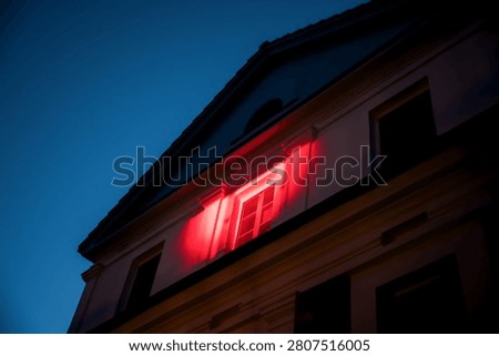 Historic manor facade dramatically illuminated with vibrant red architectural lighting against deep blue evening sky during special event