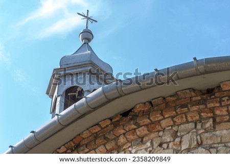 A historic old church, a bell tower with a cross (on which a bird sits).A cross on a medieval church against a blue sky with tiny clouds .