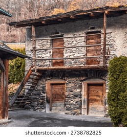 Historic Rustic Stone Barn with Weathered Wooden Balcony and Ladder in Traditional Swiss Alpine Village