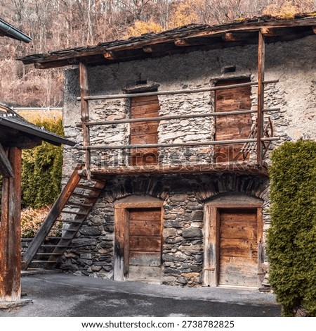 Historic Rustic Stone Barn with Weathered Wooden Balcony and Ladder in Traditional Swiss Alpine Village