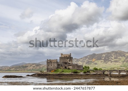 A historic Scottish stronghold, Eilean Donan Castle, connected by an elegant stone bridge, rises against the highland hills