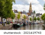 Historic ships, canal houses and warehouses on the old harbor at the Hoge der A with the tower of the historic Der Aa church in Groningen in the background.