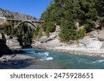 The historic Shotover Bridge over the Shotover River with a blue sky and forest background on a sunny day, in Queenstown, New Zealand