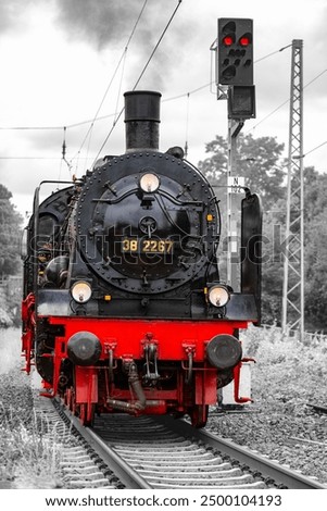 Historic steam locomotive in a curve on the railroad line between Bochum-Dahlhausen and Wetter in the idyllic Ruhr Valley, Germany. Frontal view of old train engine. Black and white with red details.