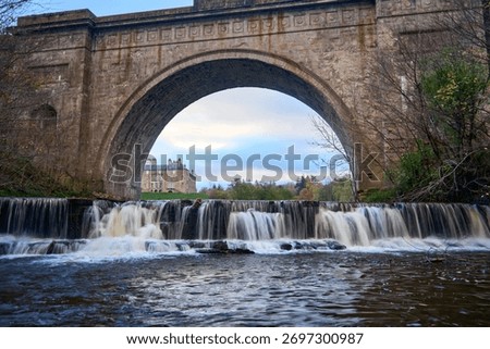 Historic stone arch frames a cascading river in Dalkeith, Scotland, bathed in soft autumn light.