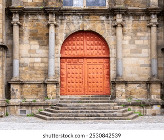 A historic stone building facade with a large, ornate wooden door and stone steps leading up to it. - Powered by Shutterstock