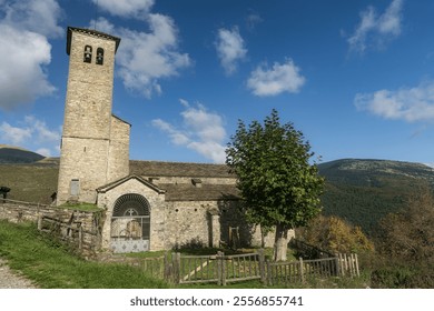 A historic stone church with a bell tower, surrounded by greenery and set against a bright blue sky and mountainous backdrop in Fanlo. - Powered by Shutterstock