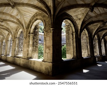 Historic stone cloister with arches and sunlight filtering through, creating intricate shadows. - Powered by Shutterstock