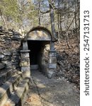 Historic stone springhouse nestled in a wooded area, surrounded by natural rock formations and forest foliage, capturing rustic charm and timeless architecture.