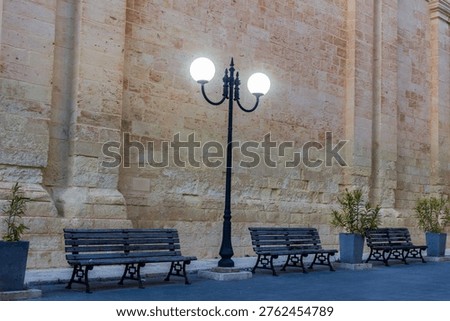 Historic Stone Wall With Lamppost and Empty Benches Along Quiet Urban Street at Dusk