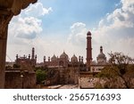 Historic view of the Badshahi Mosque in Lahore, Pakistan, framed by old city architecture, under a partly cloudy blue sky, showcasing Mughal-era grandeur and timeless heritage.
